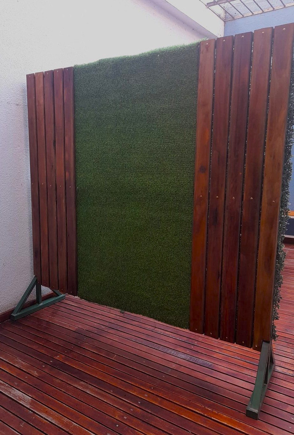 Panel vertical de listones de madera con tramo central de césped artificial sobre bases metálicas