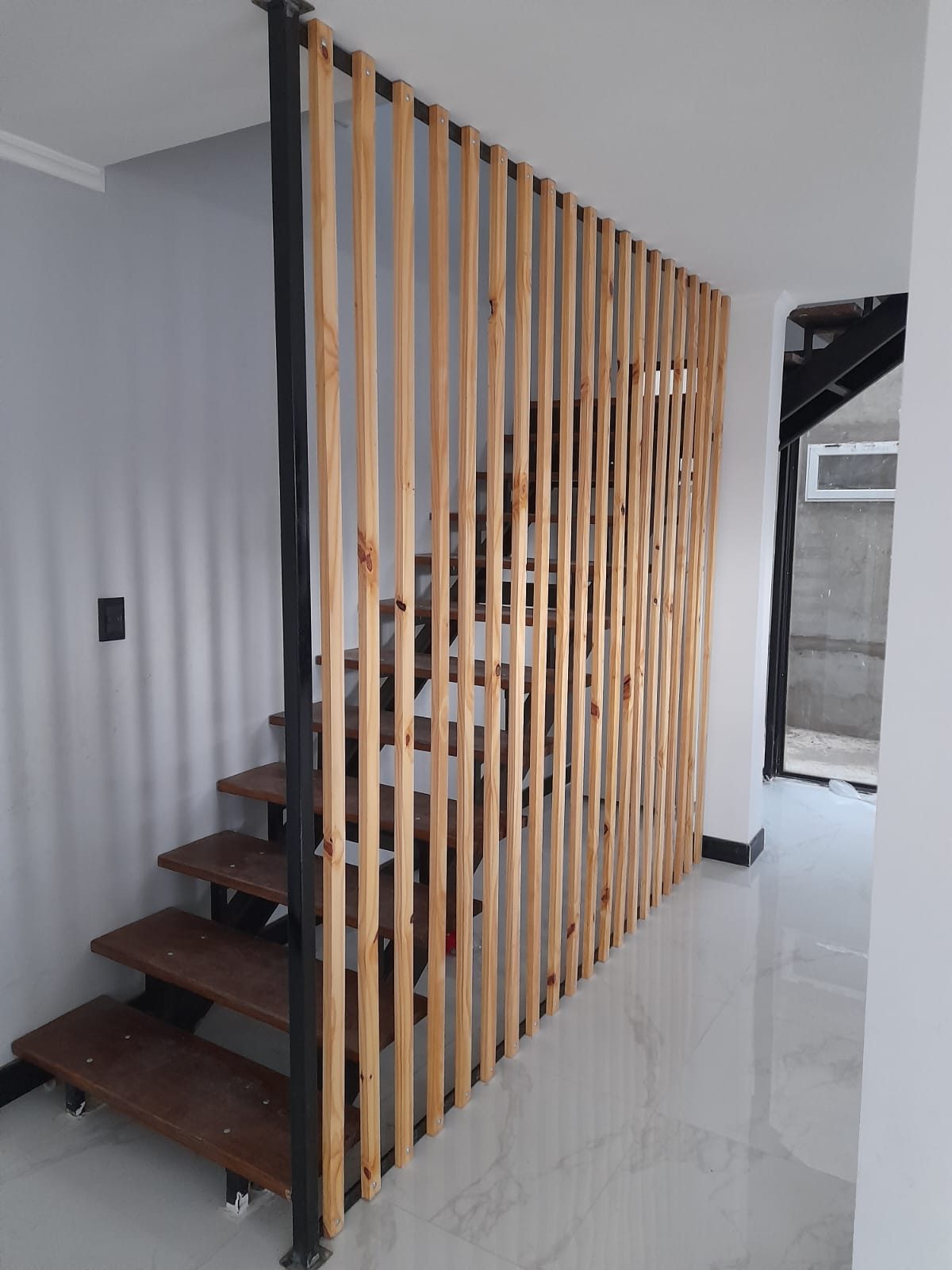Divisor de listones de madera junto a una escalera con estructura metálica