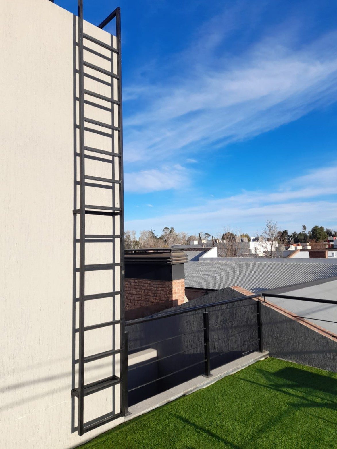 Escalera metálica fija y baranda negra en una terraza con césped artificial