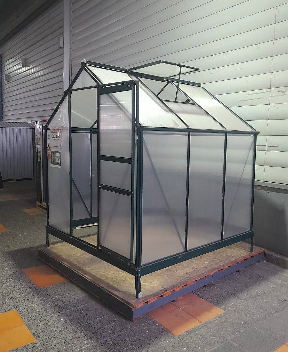 Invernadero de perfilería metálica verde con placas traslúcidas y puerta corrediza abierta