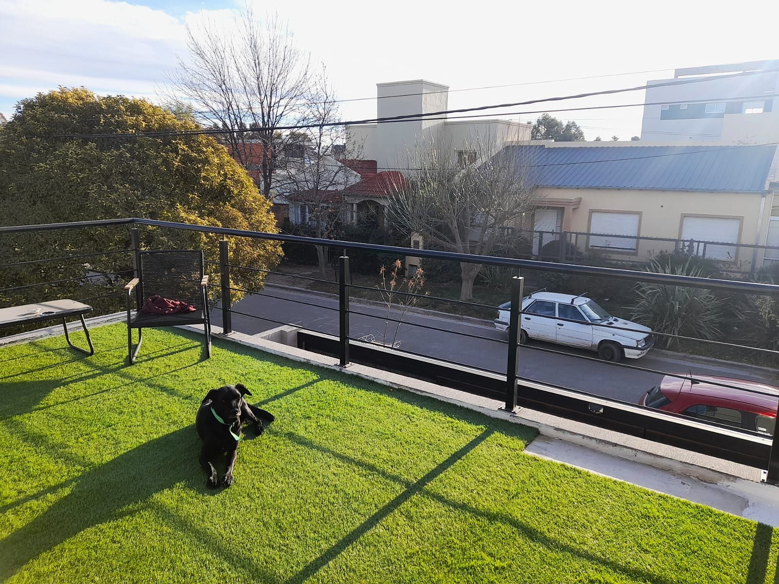 Terraza con césped artificial y baranda metálica negra sobre la calle